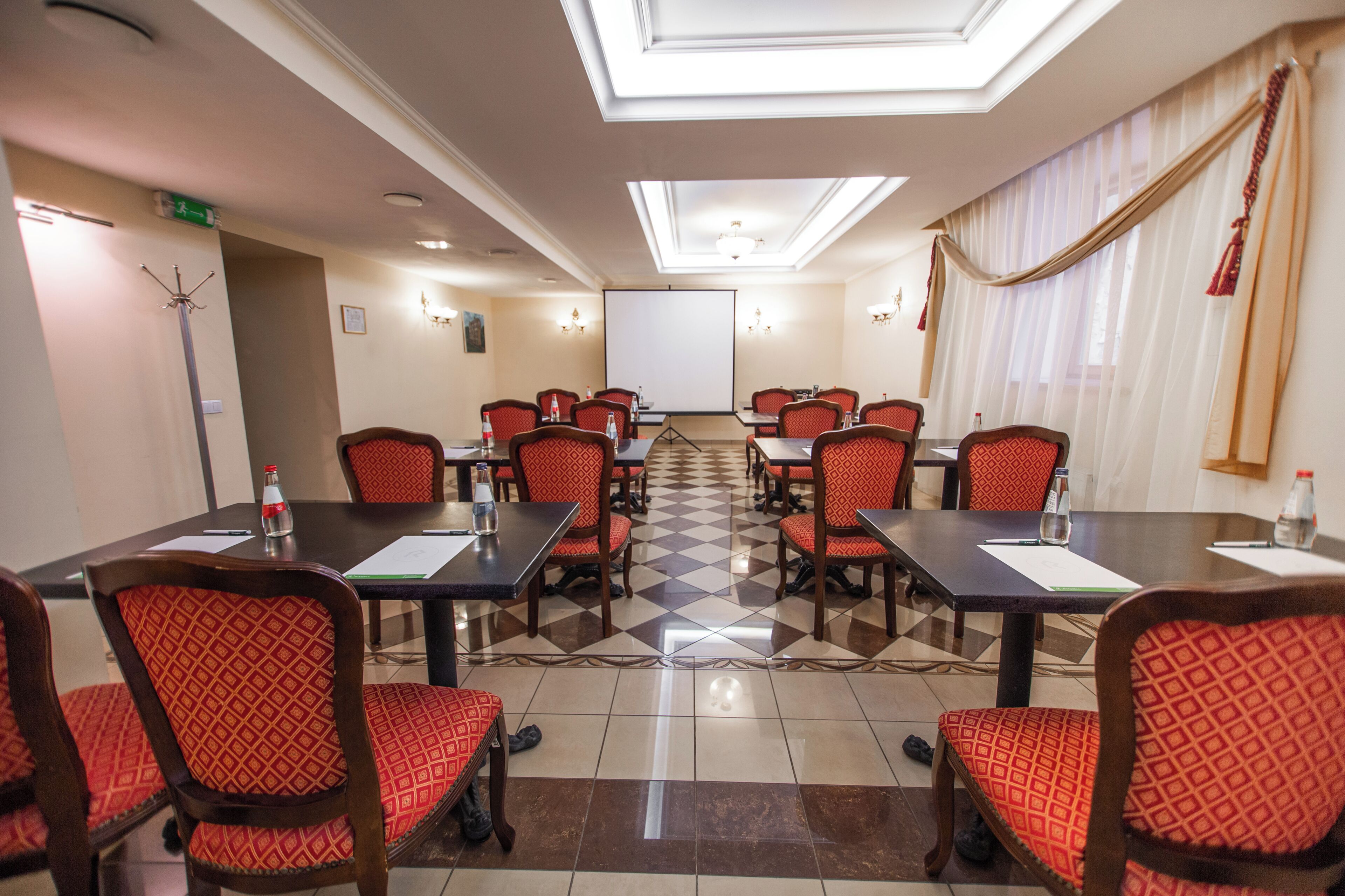 A conference room with a checkered floor, red patterned chairs, and a large screen at the front.