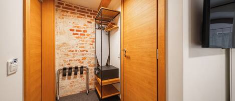 A narrow hallway with a brick wall, wooden doors, a ceiling light, and a black TV mounted on the wall.