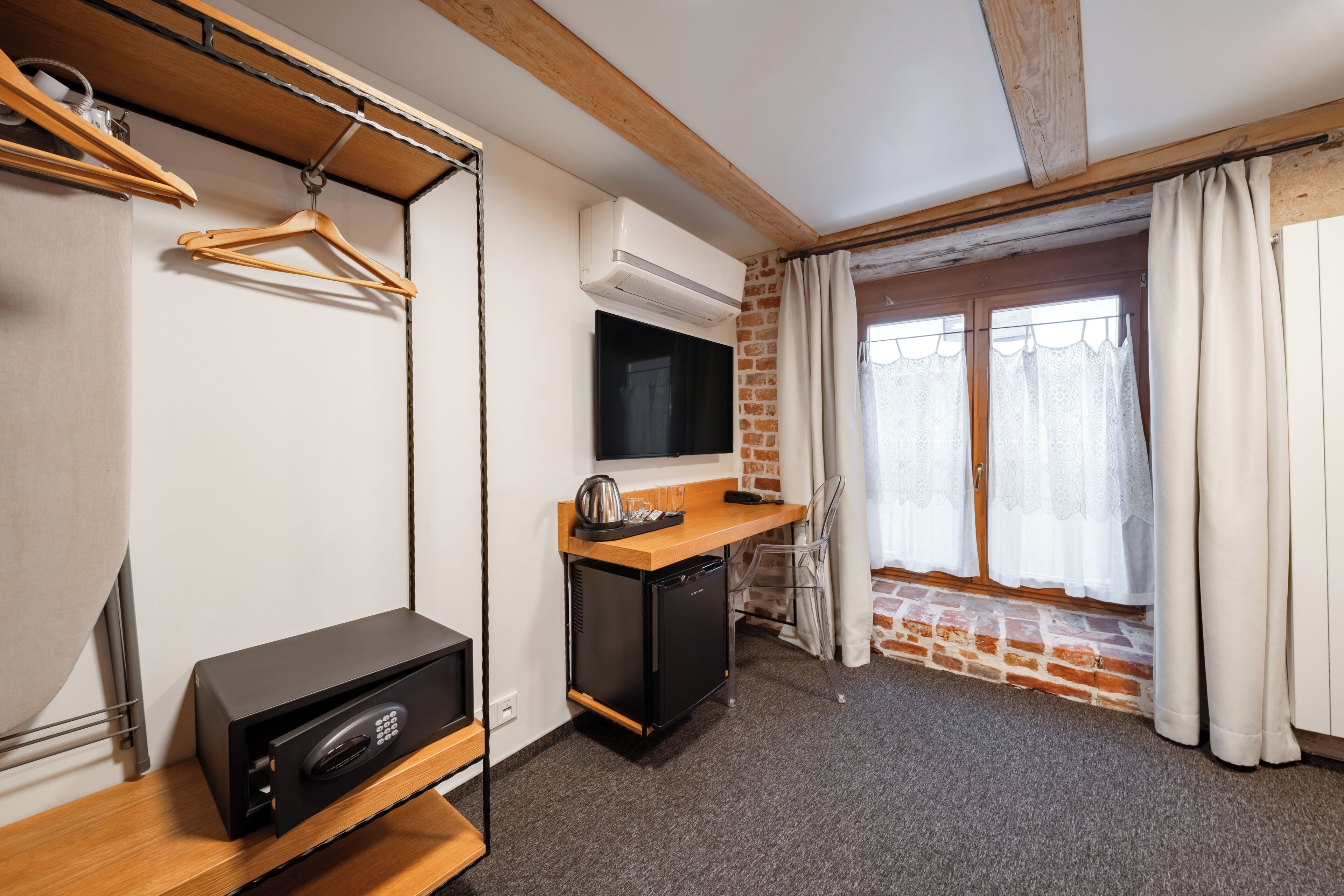 Una habitación compacta con kitchenette, televisor, perchero y ventana con cortinas.