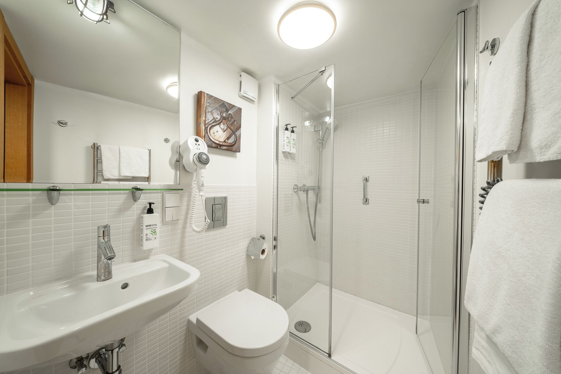 A modern bathroom with a glass shower enclosure, a white sink, a toilet, and a hairdryer mounted on the wall.