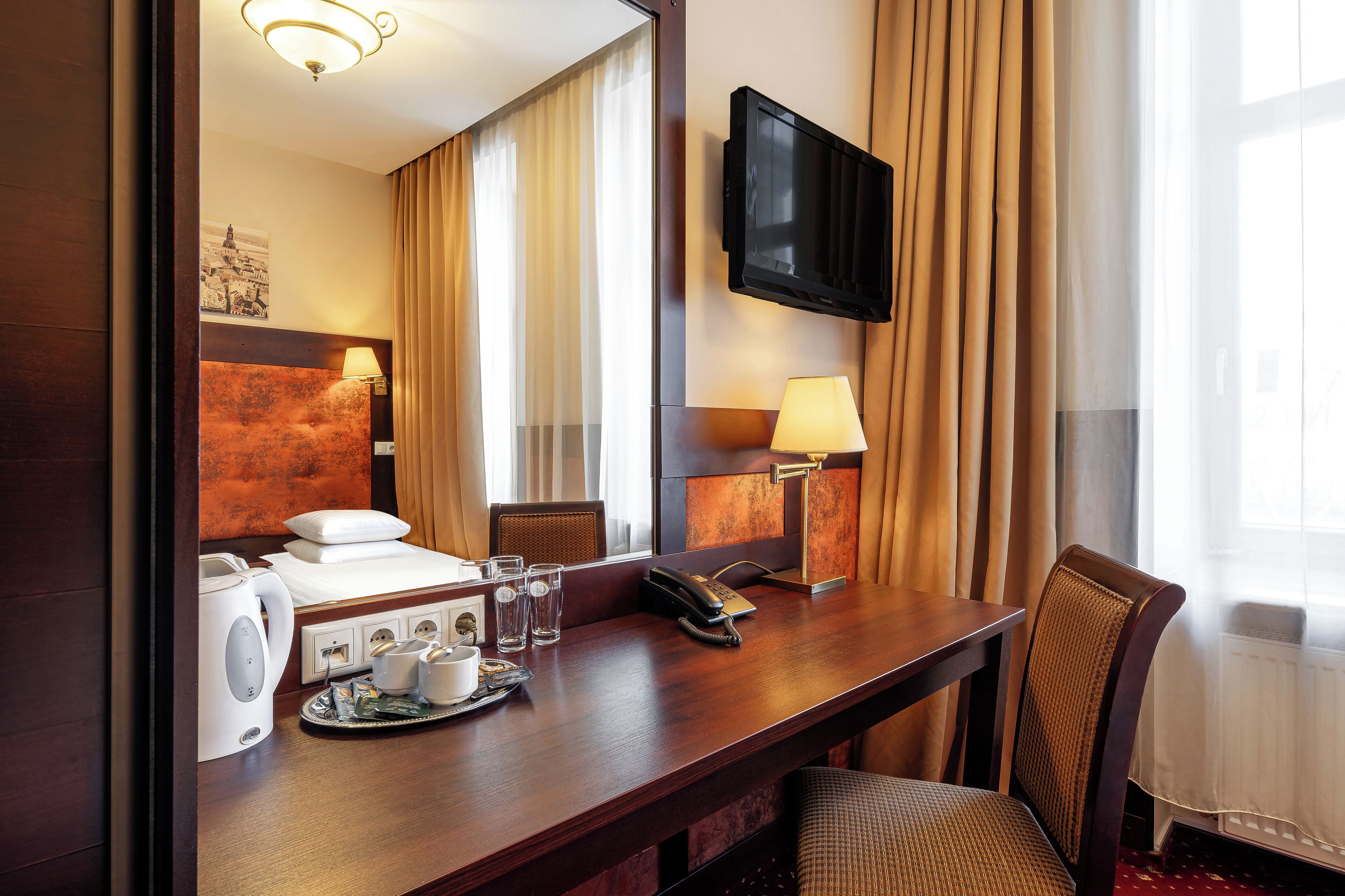 A hotel room with a bed, a desk with a telephone, a television, and a window with curtains.