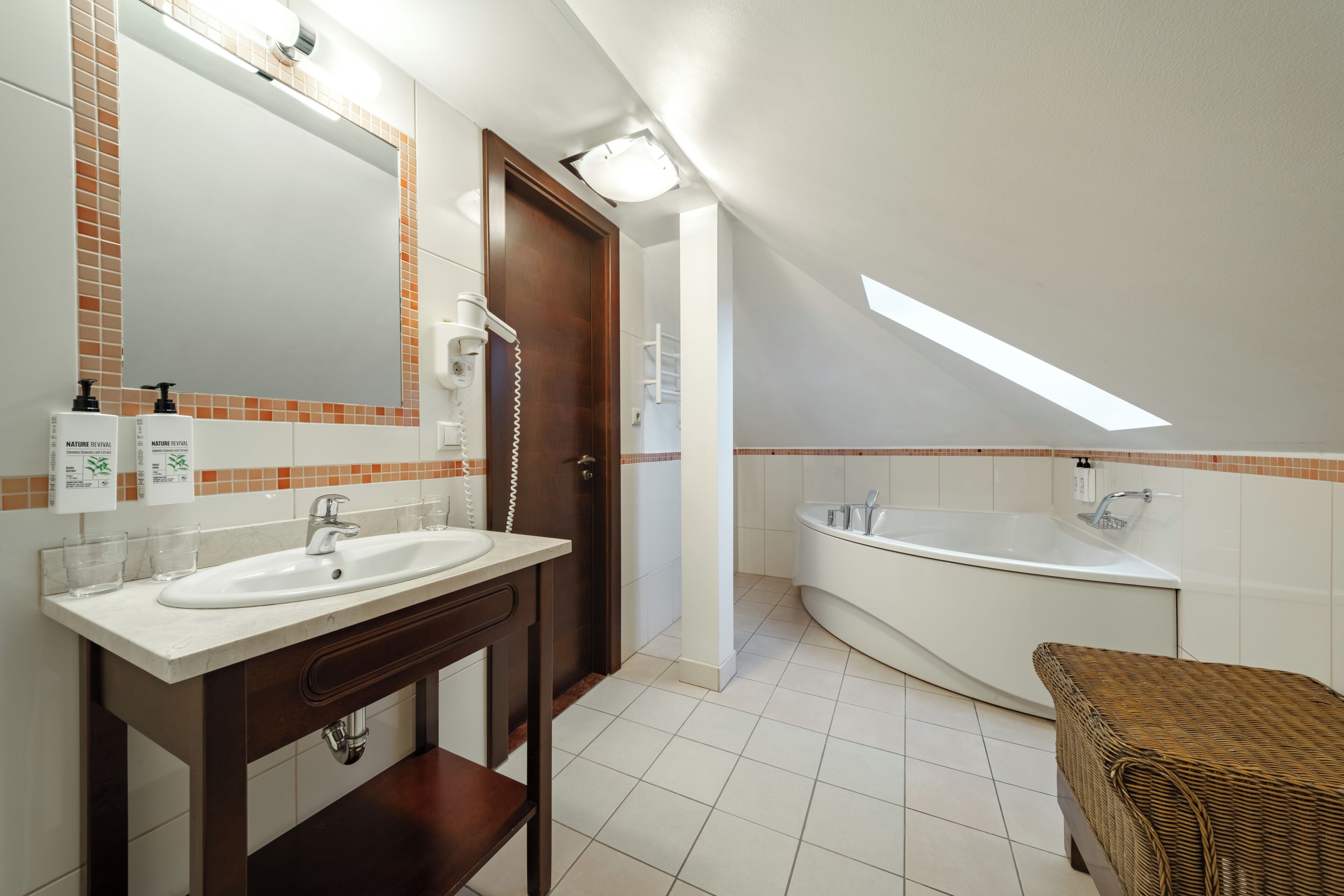 A modern bathroom with a dual sink vanity, a large mirror, a freestanding bathtub, and a skylight.