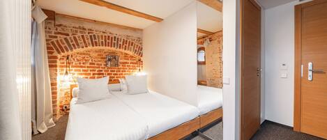 A room with a bed, a brick wall, wooden beams, and a door.