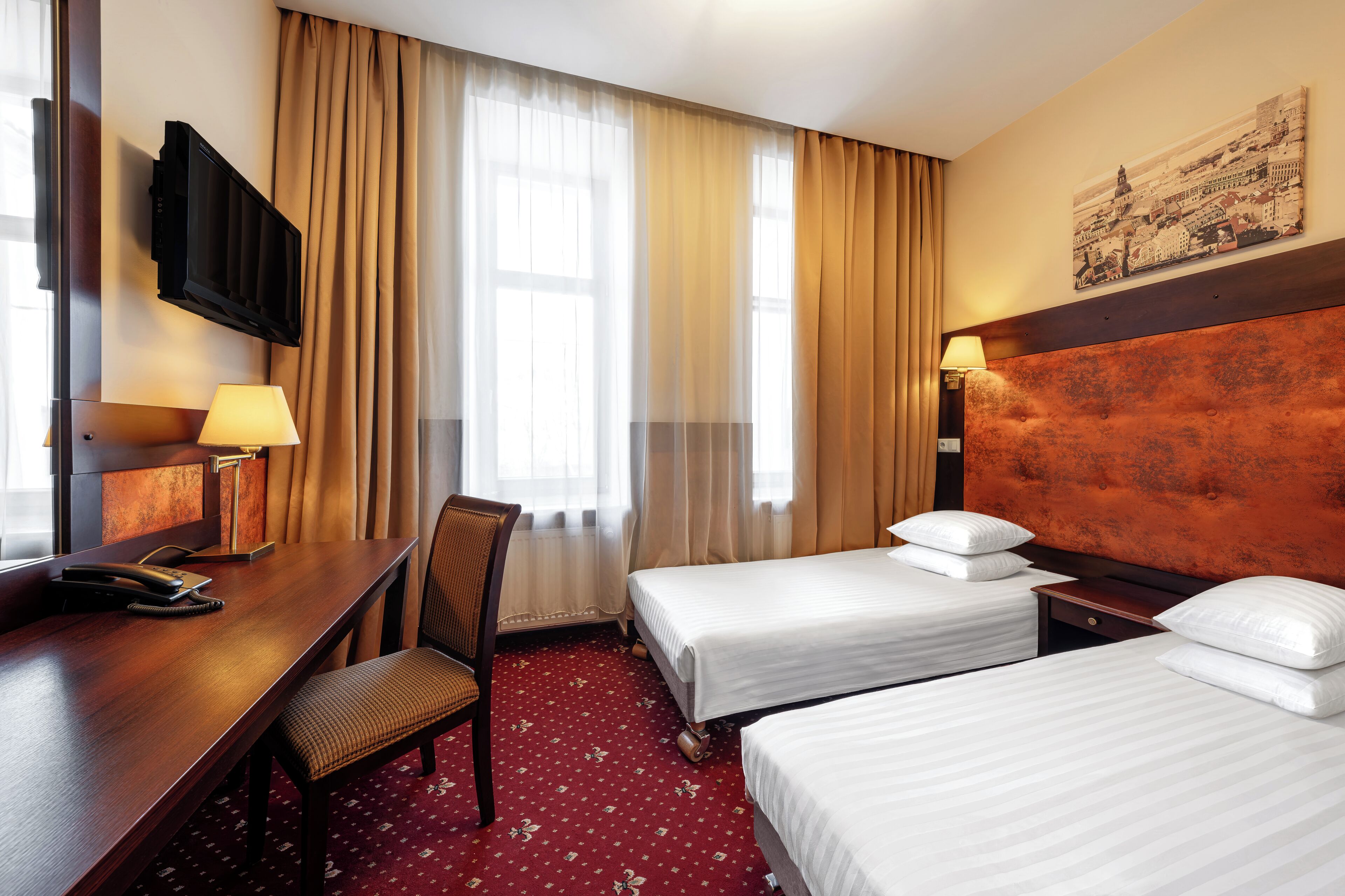 Ein Hotelzimmer mit Schreibtisch, zwei Einzelbetten, einem Sessel, einem Fernseher und einem Bild an der Wand.