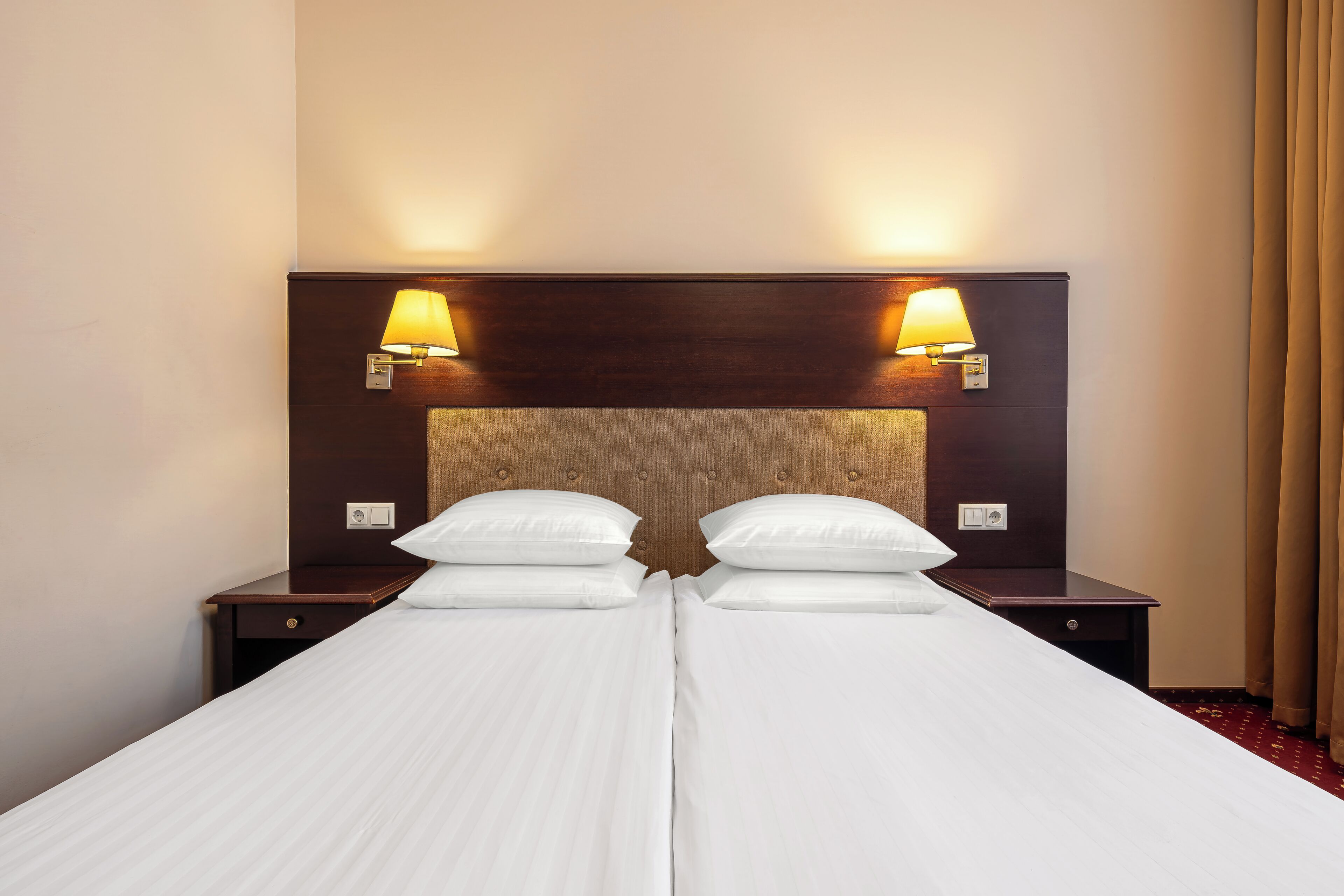A double bed with two bedside tables, each with a lamp, in a hotel room.