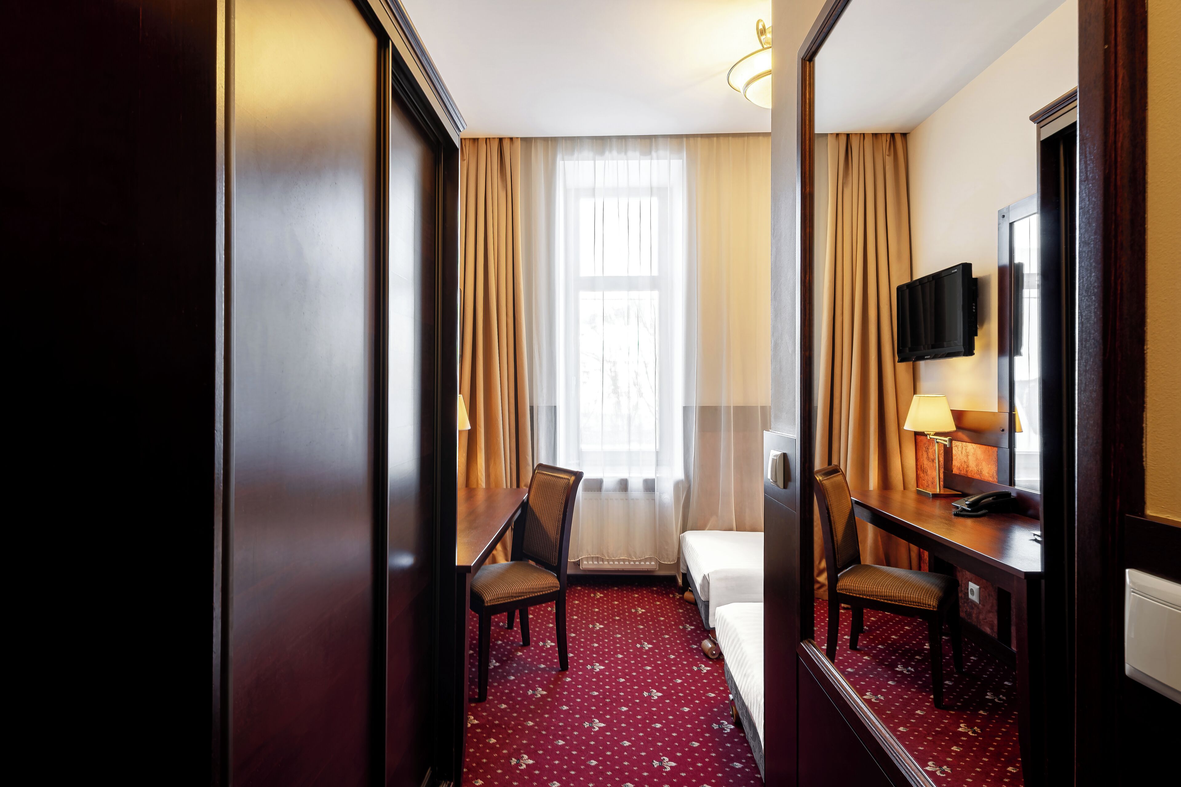 A hotel room with a bed, two chairs, a desk, a television, and a window with curtains.