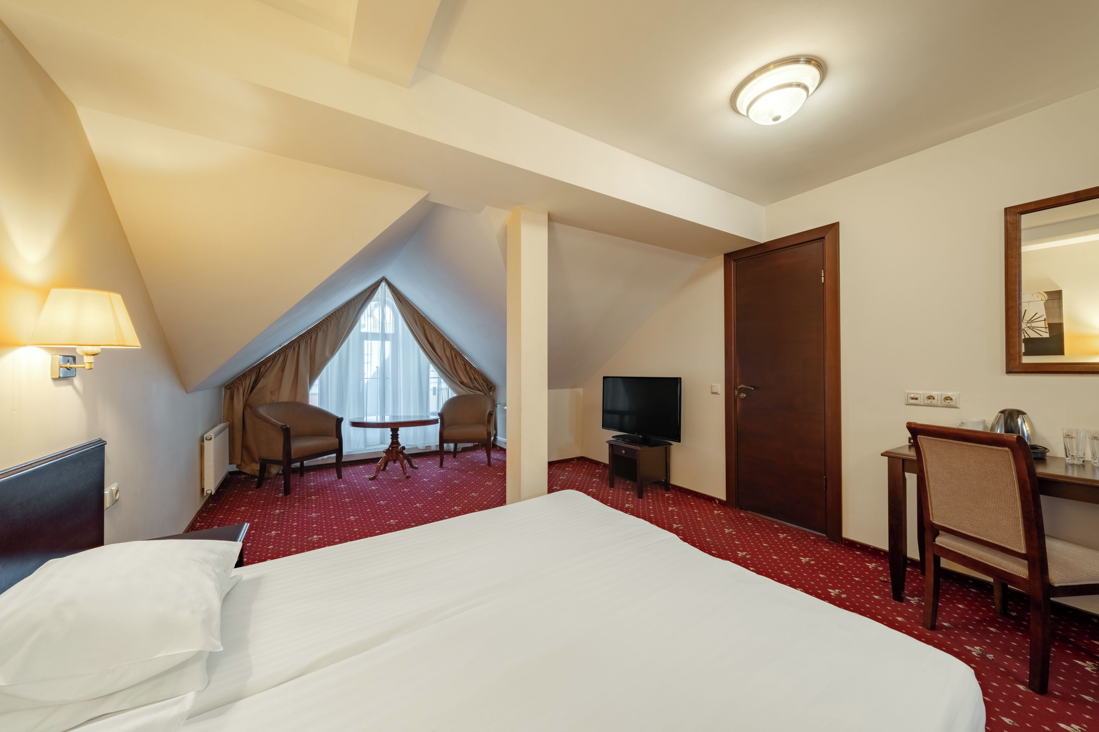 A hotel room with a large bed, a desk with a chair, a television, and a window with curtains.