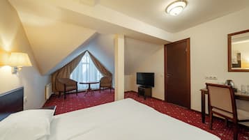 A hotel room with a large bed, a desk with a chair, a television, and a window with curtains.