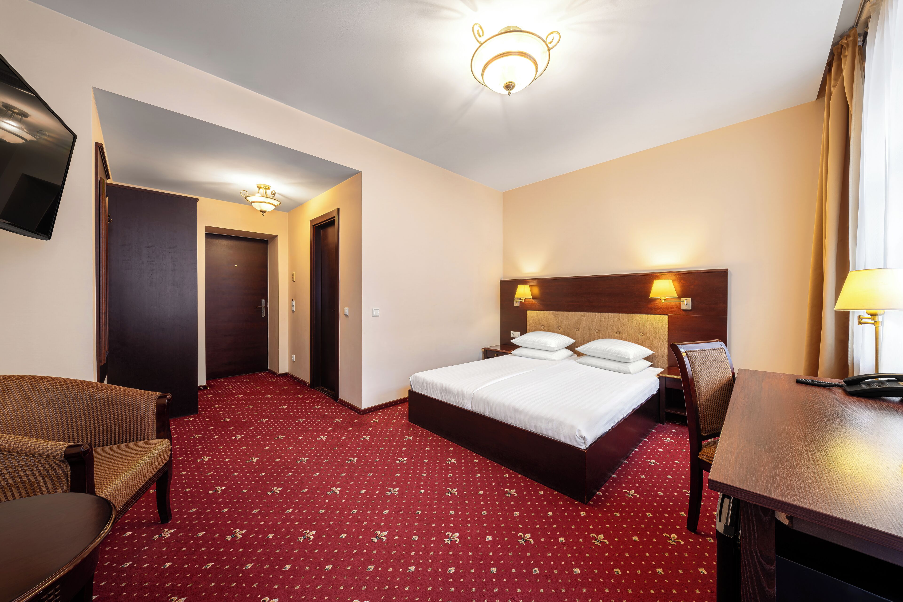 A hotel room with a bed, a desk, a chair, a TV, and a door.