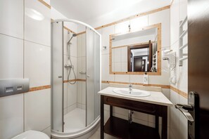 Un baño moderno con ducha separada por mampara de vidrio, lavamanos con espejo y toallero.