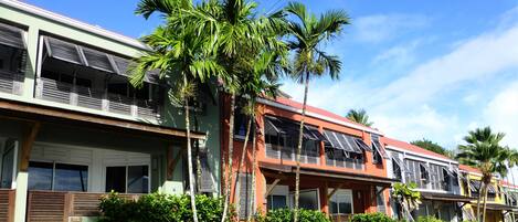 A row of multi-story buildings with balconies, palm trees, and a clear blue sky.