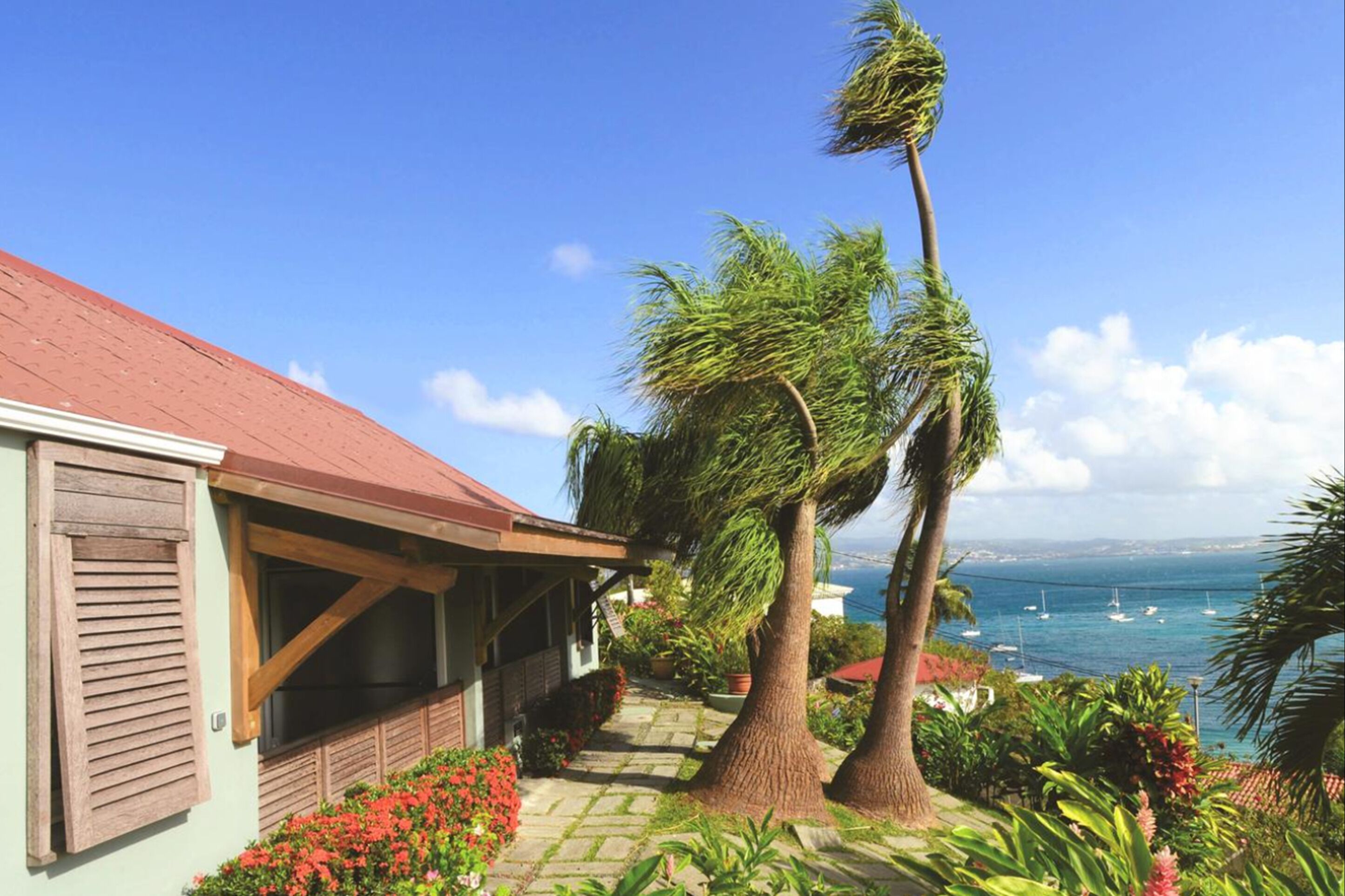 A house with a red roof, a covered porch, and a view of the sea with boats.