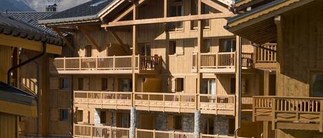 A multi-story wooden building with balconies, stone walls, and a mountain backdrop.