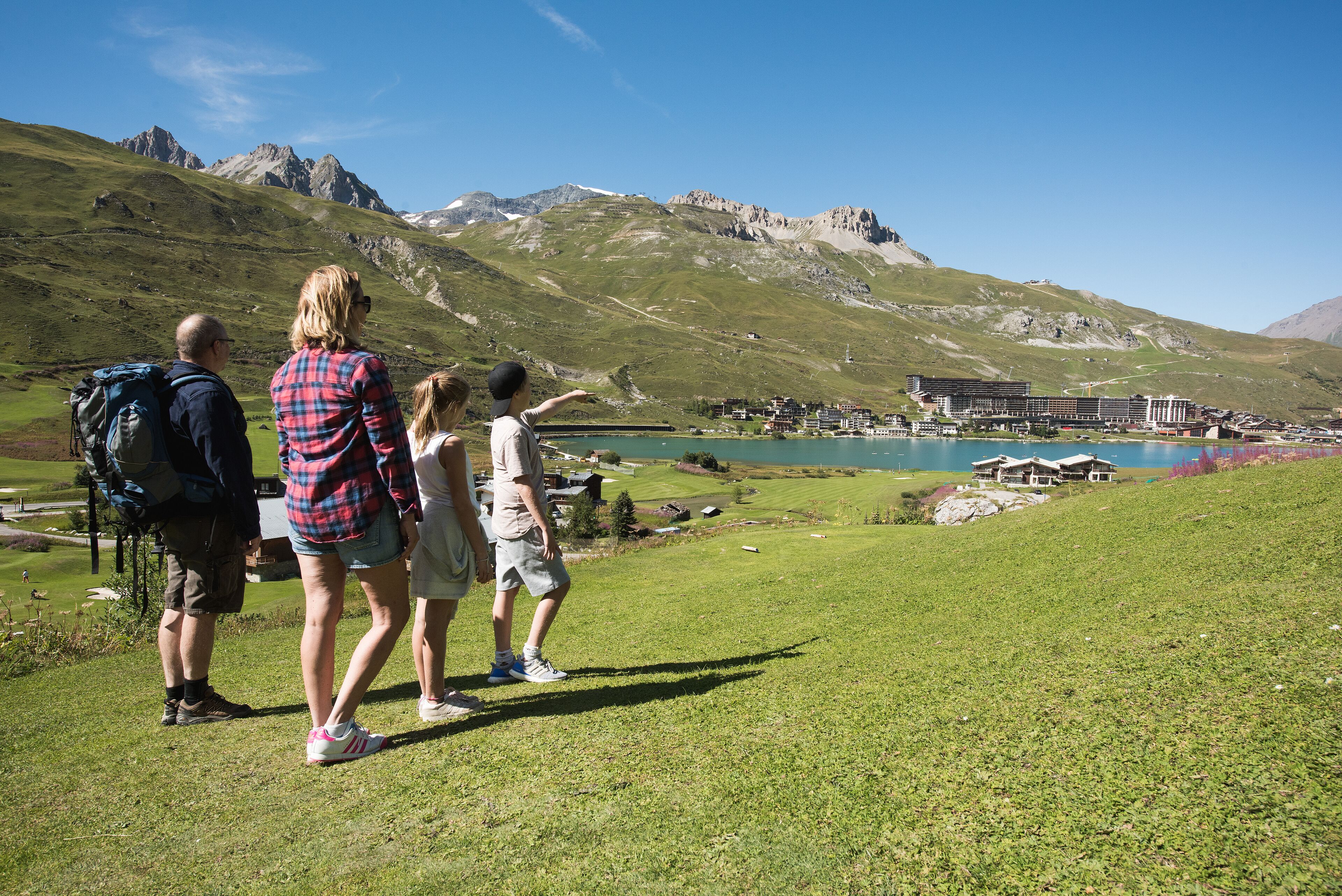 A family standing on a grassy hill overlooking a lake and mountains.
