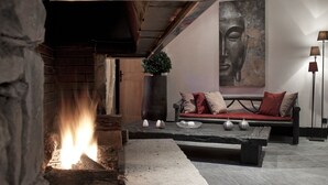 Un salon moderne avec une cheminée en pierre, un canapé avec des coussins et un tableau représentant un Bouddha accroché au mur.