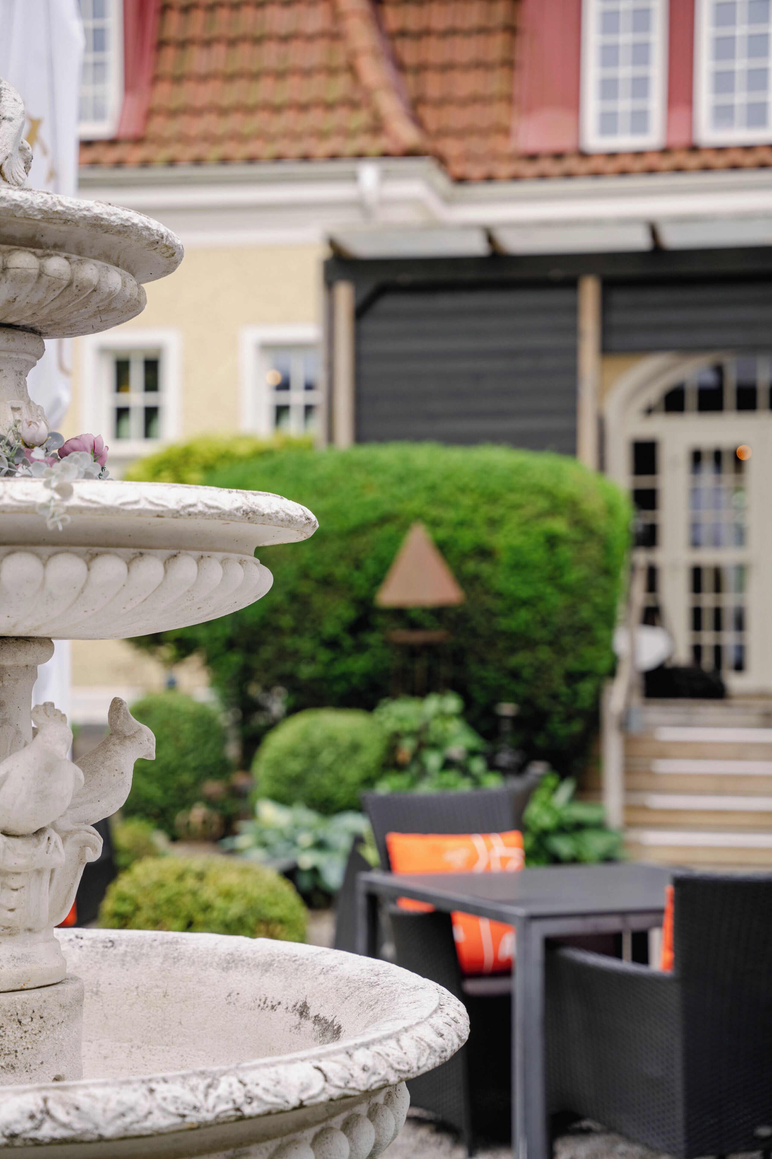 A stone fountain, outdoor seating, and a well-maintained hedge in a courtyard.