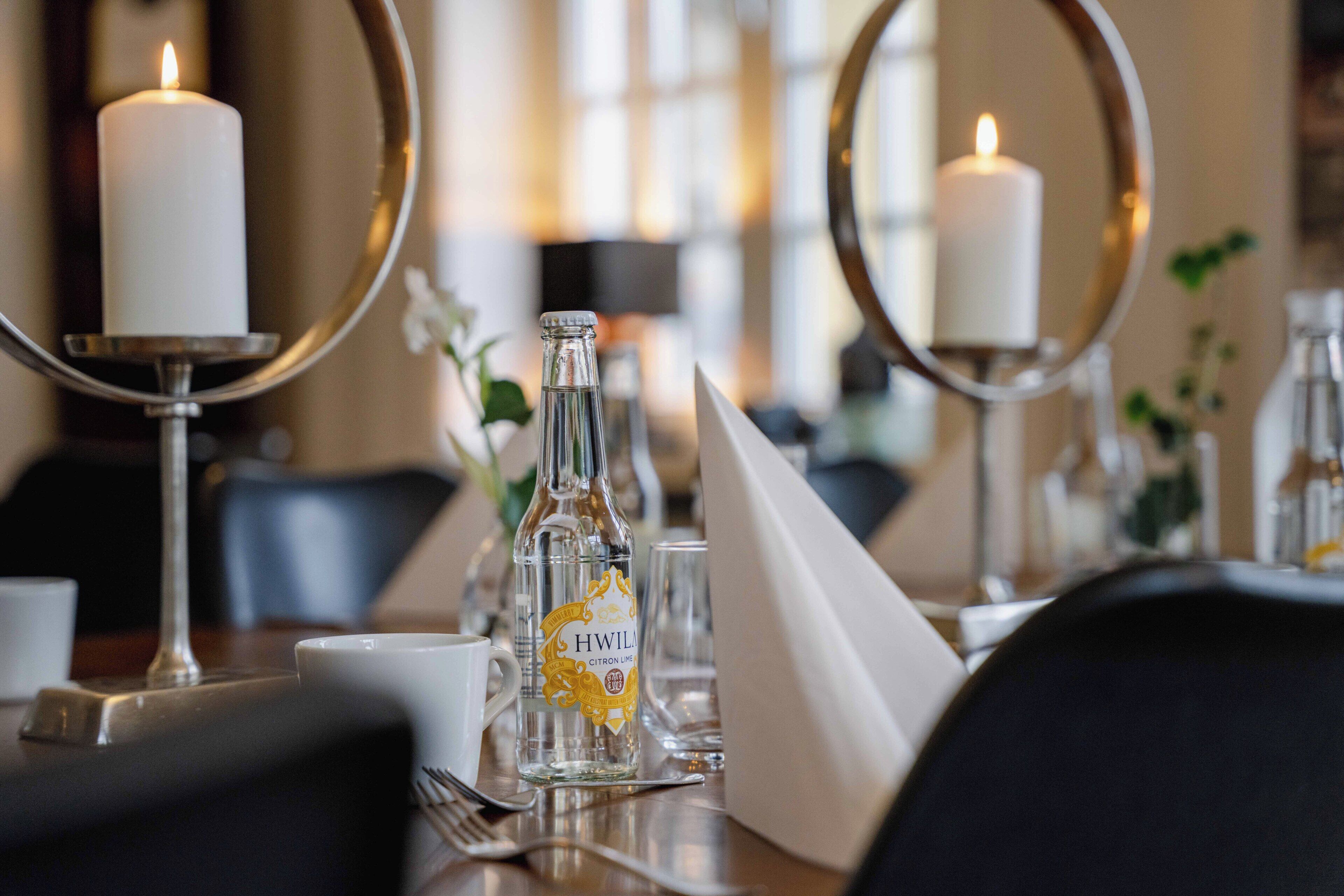 A dining table with candles, a bottle of H.WILA Citron Liqueur, and a mirror.