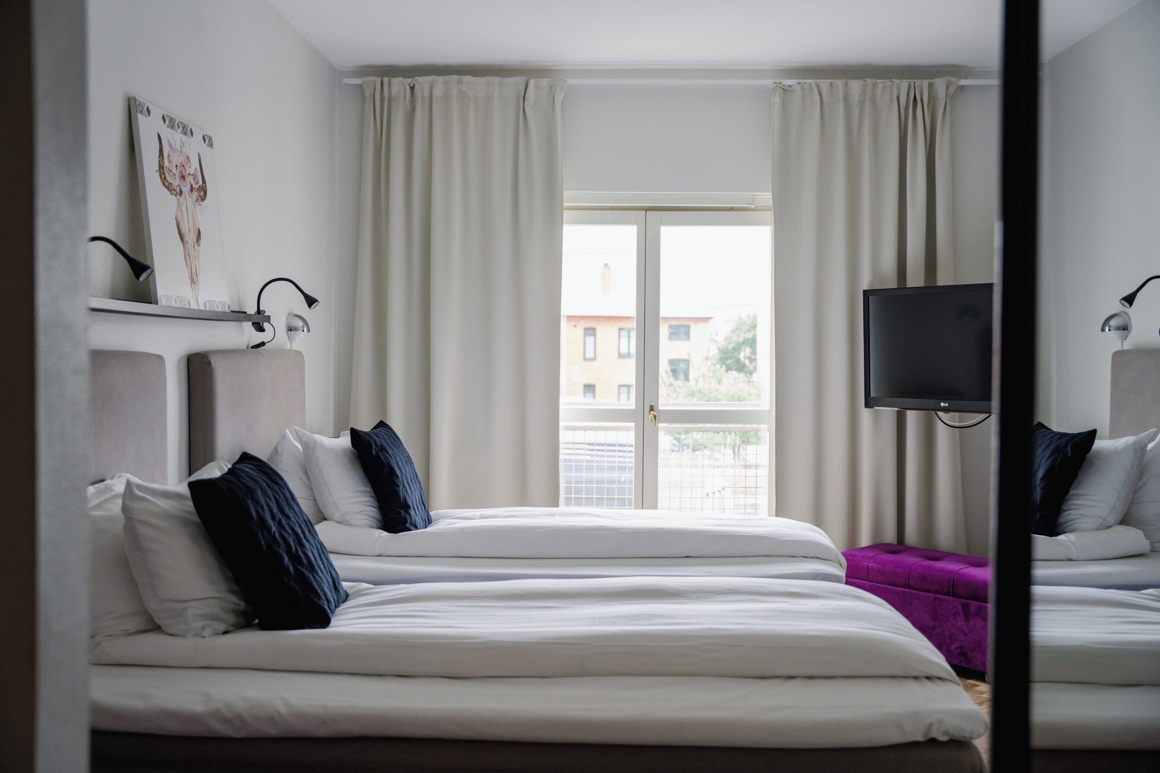 Une chambre d’hôtel avec deux lits, une télévision et une fenêtre avec des rideaux.