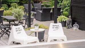Un área de estar al aire libre con dos sillas blancas, una con el texto 'HA EN BRA DAG!' y la otra con 'KOPPLA AV HÅR!'.