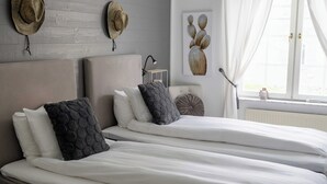 Una cama doble con ropa de cama blanca, dos almohadas, una mesita de noche con lámpara y un perchero de pared.