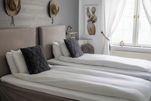 A double bed with white bedding, two pillows, a bedside table with a lamp, and a wall-mounted hat rack. - Hotel Dannegården Trelleborg (Trelleborg)