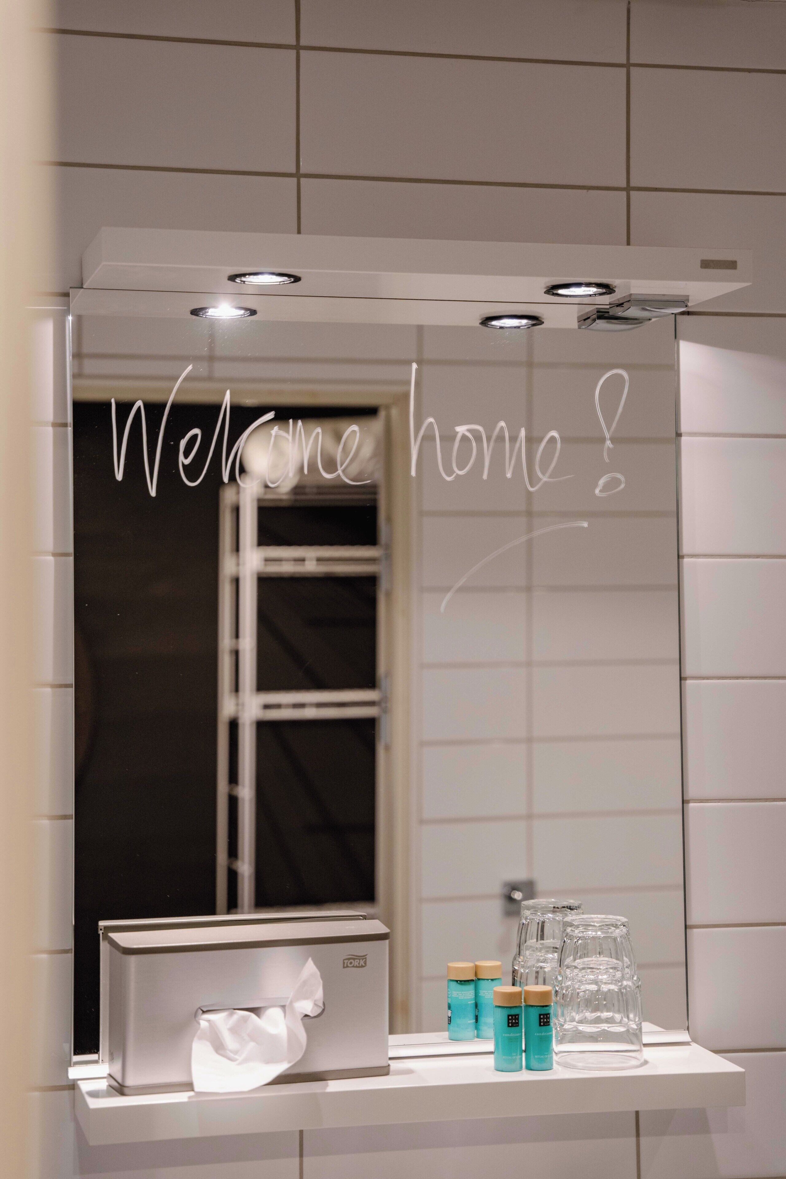 Un bagno con uno specchio, un dispenser per asciugamani e uno scaffale con prodotti per l'igiene personale.