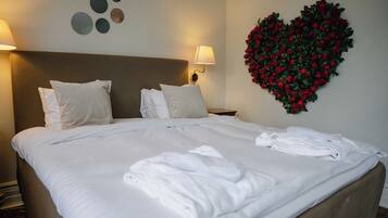 Ein ordentlich bezogenes Bett mit weißen Leinen und Kissen, eine herzförmige Blumenleiste an der Wand und zwei Wandleuchten mit Lampen.