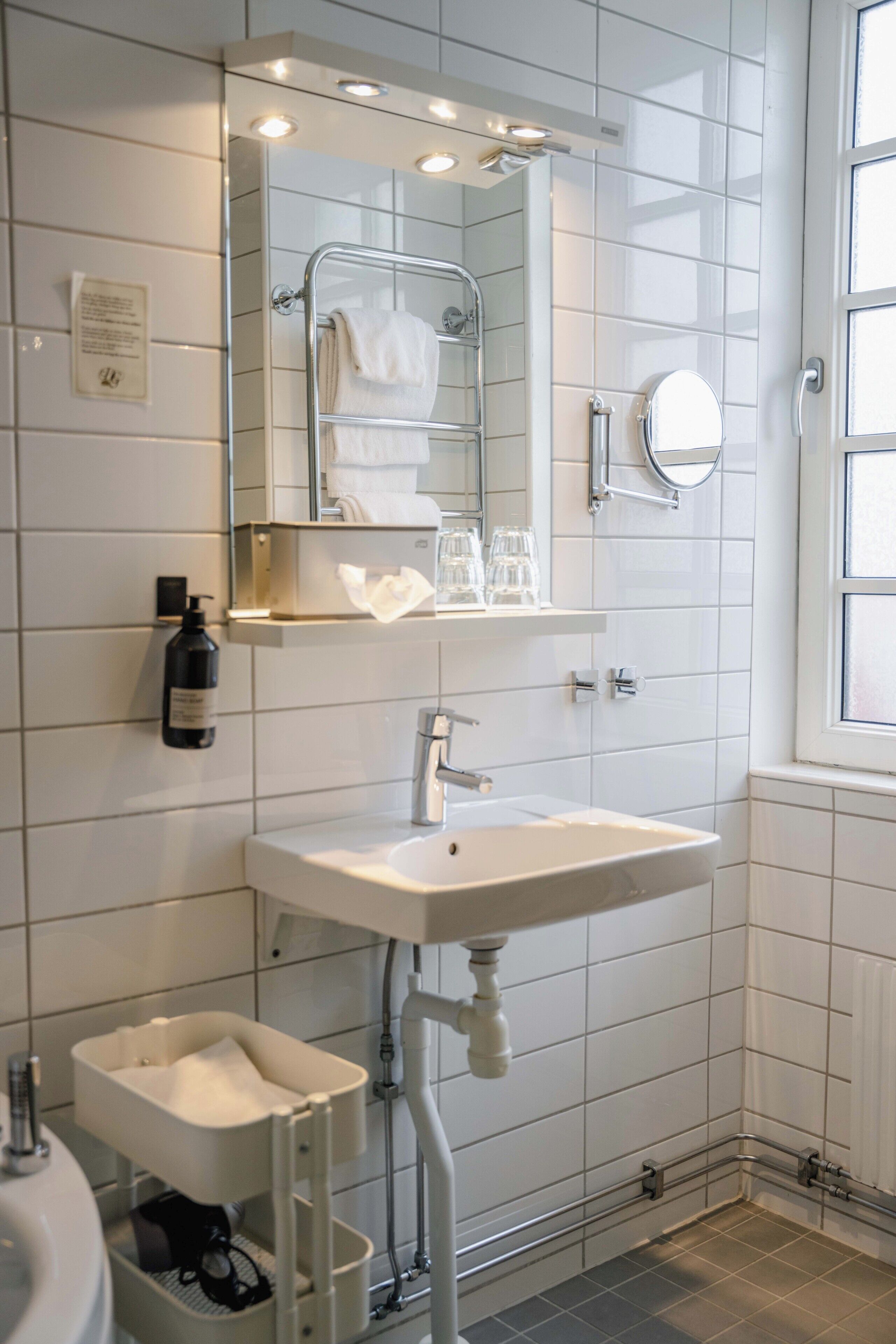 Ein modernes Badezimmer mit Waschbecken, Spiegel, Handtuchhalter und einem Fenster.