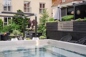 Un espace extérieur avec une piscine, des sièges, une pergola et un jeu de fléchettes.