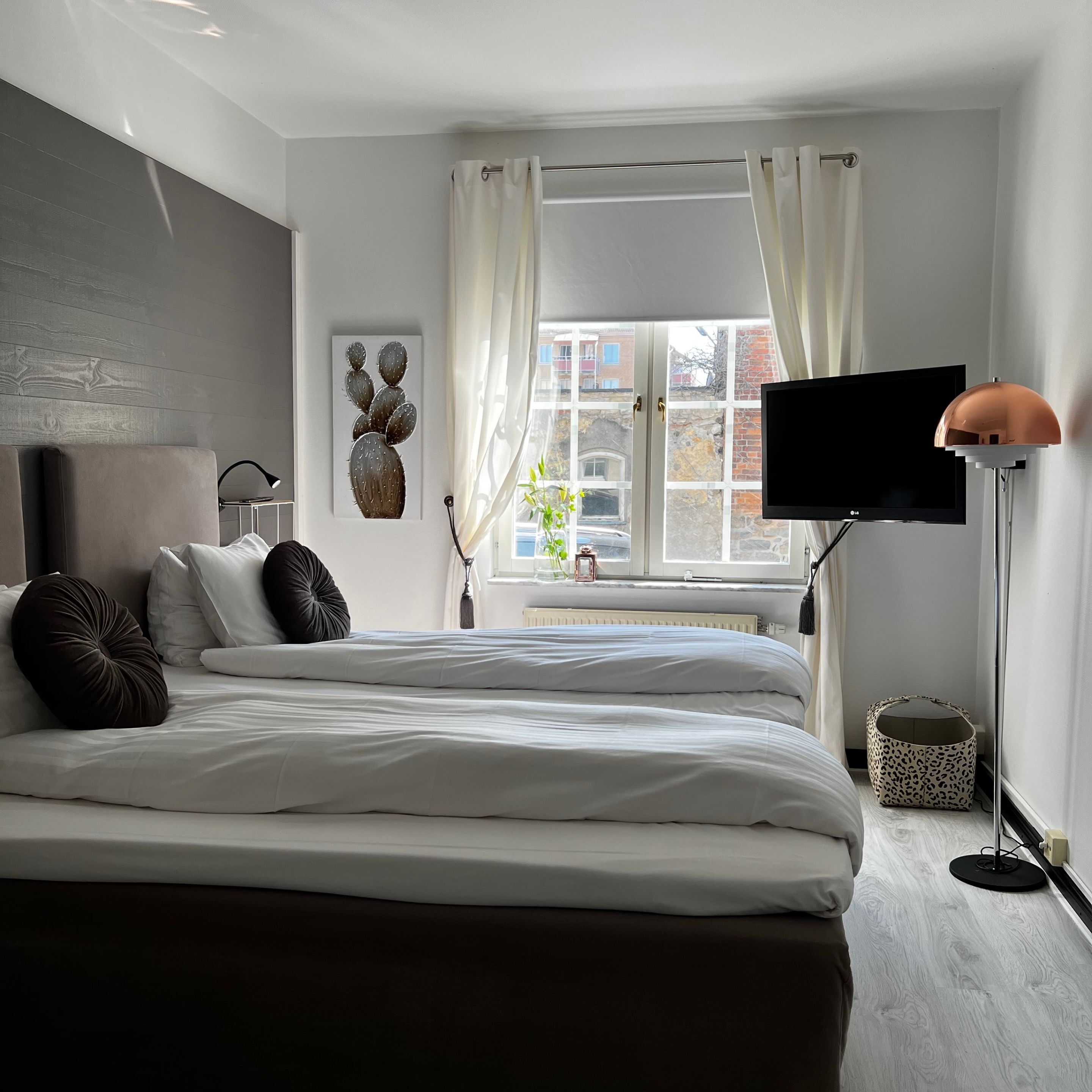 A modern bedroom with a large bed, a flat-screen TV, a floor lamp, and a window with curtains.
