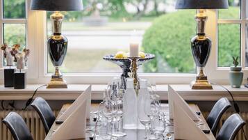 A dining table set with glasses and a candle, flanked by two lamps, in a room with a large window.