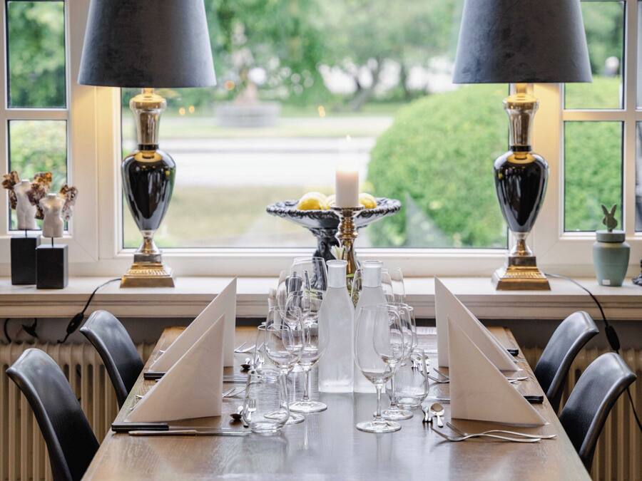 A dining table set with glasses and a candle, flanked by two lamps, in a room with a large window.