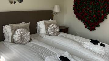 Una cama bien hecha con sábanas blancas, un arreglo floral con forma de corazón en la pared y una mesita de noche con lámpara.