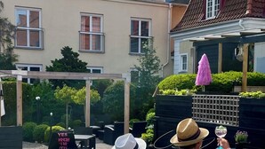 A swimming pool with a pergola, a pink umbrella, and a building in the background. - Hotel Dannegården Trelleborg (Trelleborg)