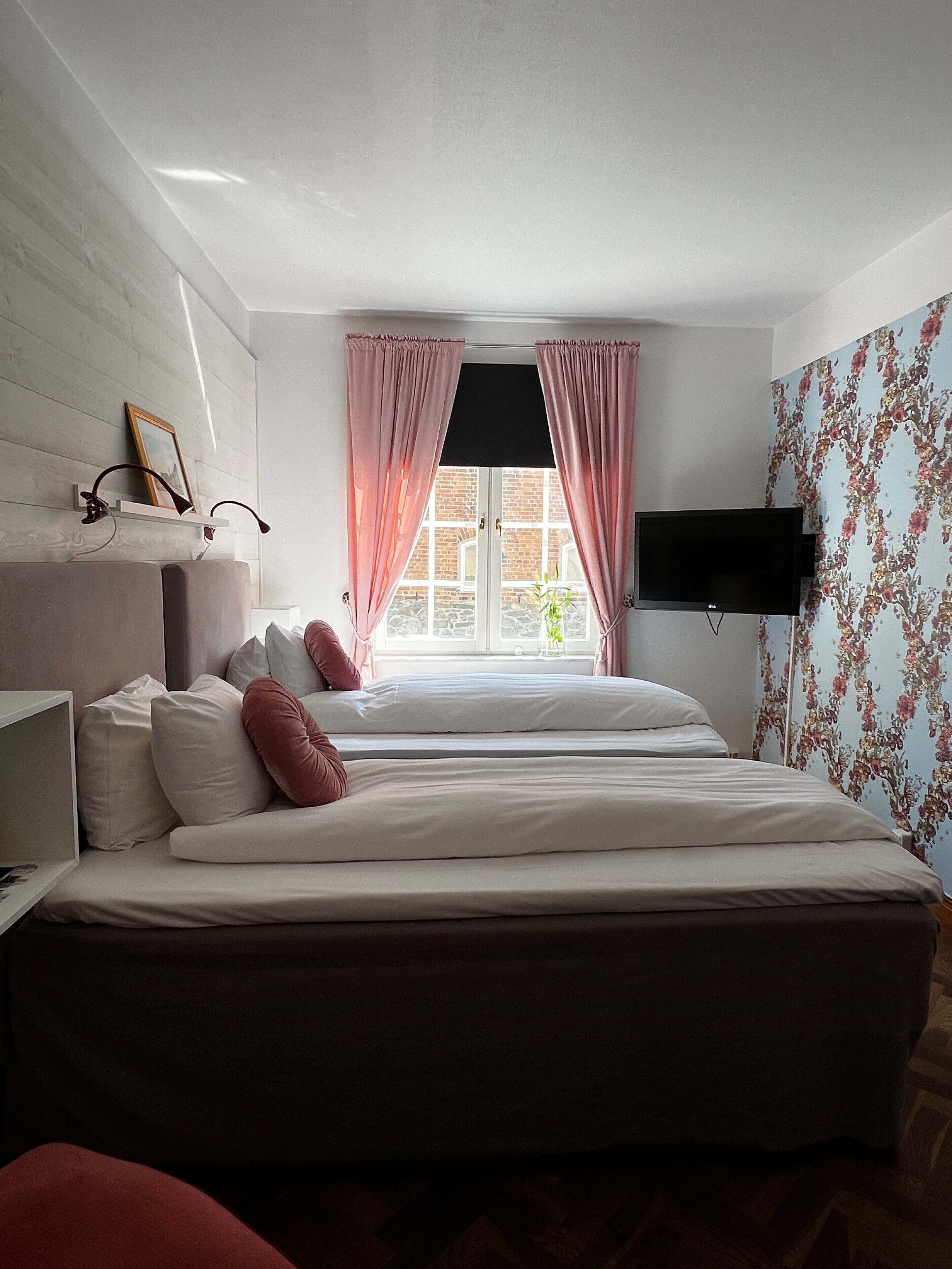 Ein Schlafzimmer mit zwei Betten, einem Fernseher und einem Fenster mit Vorhängen.