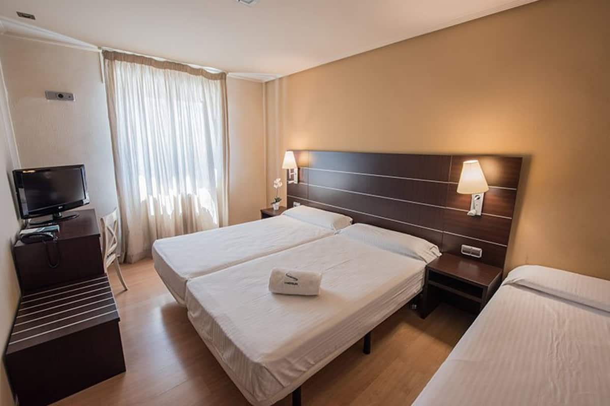 A hotel room with two beds, a TV, a desk, and a window with curtains.