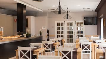 Un restaurante con mesas y sillas de madera, una barra con comida y luces colgantes.