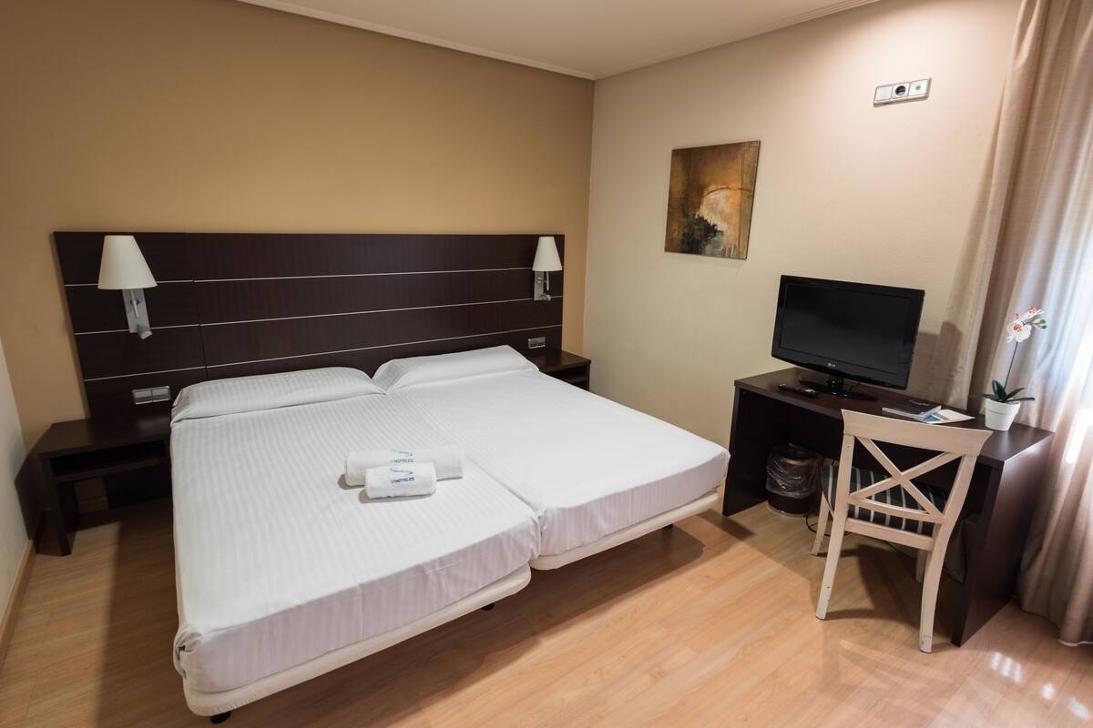 A hotel room with a large bed, a desk with a TV, and a small chair.