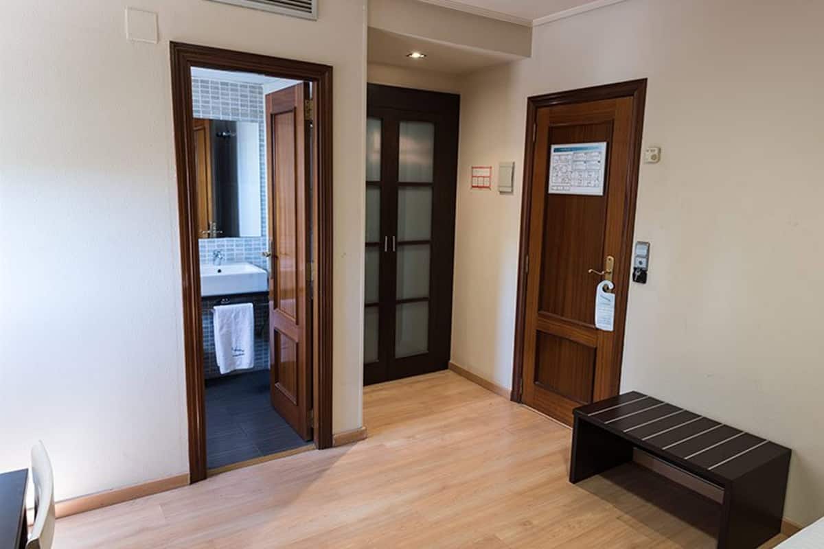 A hallway with wooden flooring, a bench, and a door leading to a bathroom with a sink and towel.