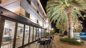 An outdoor cafe area with tables and chairs, a palm tree, and a building with a sign reading "Las Ventas". - Hotel Las Ventas (Utebo)