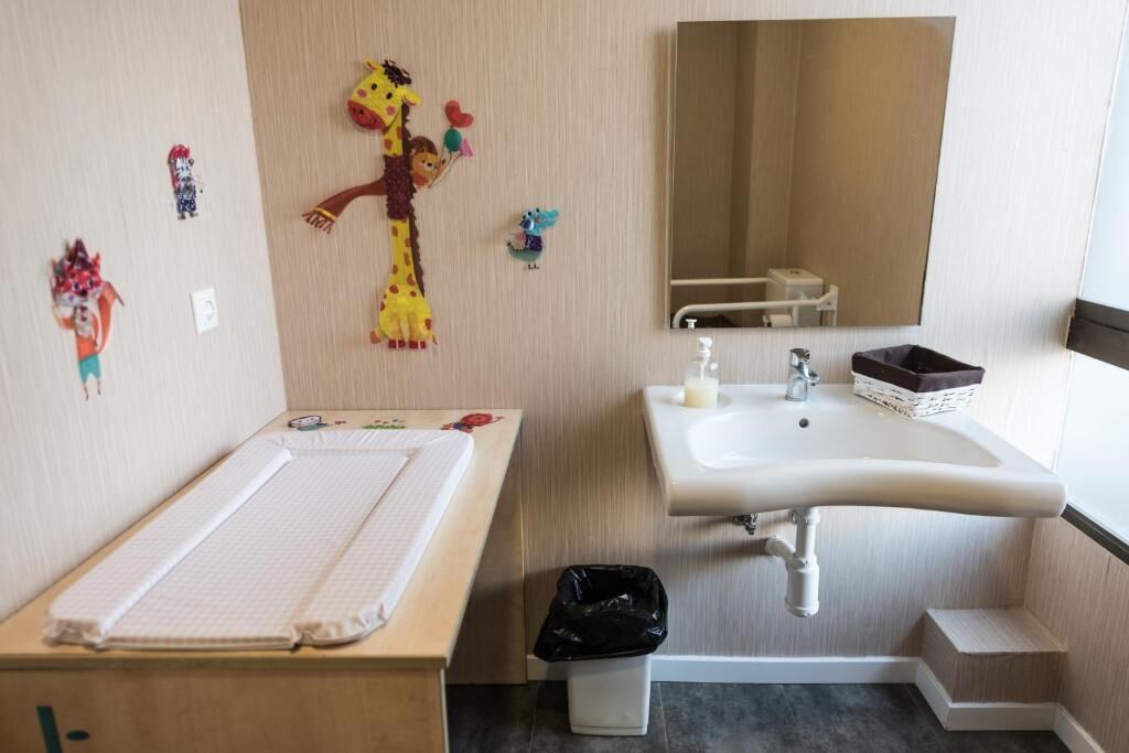 A bathroom with a sink, mirror, and a small trash bin.