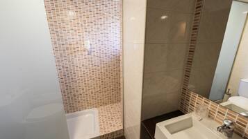Een badkamer met een betegelde douche, een wastafel en een spiegel.