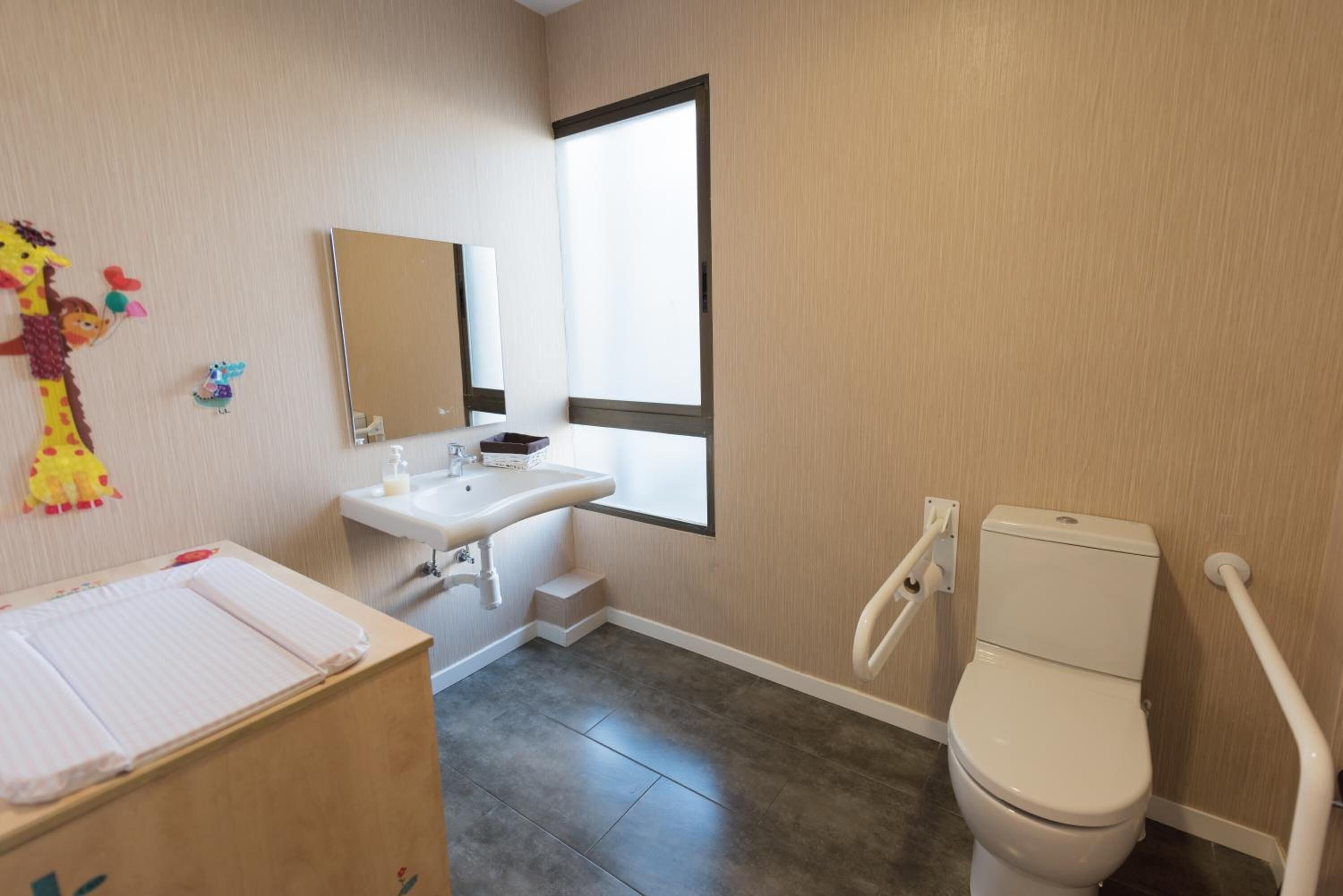 A bathroom with a toilet, sink, and mirror. There is a window providing natural light.