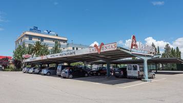 A hotel parking lot with multiple cars parked under a covered area.