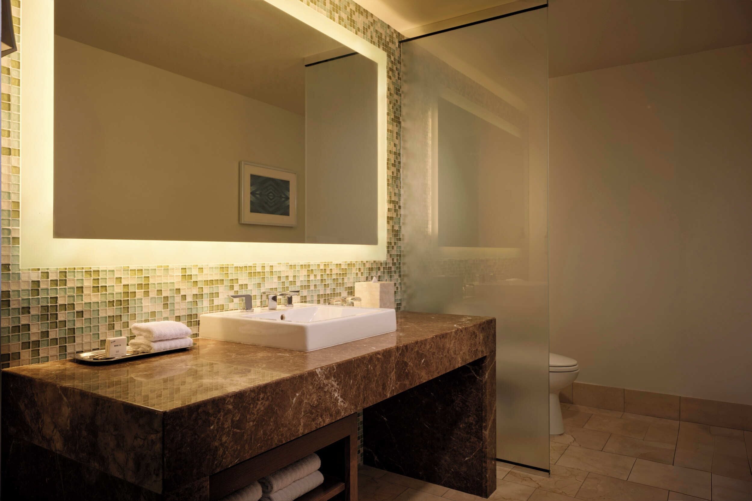 Un baño con lavamanos de mármol, un espejo grande y cabina de ducha con paredes de vidrio.
