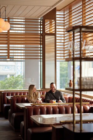A restaurant with wooden slatted walls, leather booths, and a large window offering a view of the city. - Fairmont Pittsburgh (Pittsburgh)
