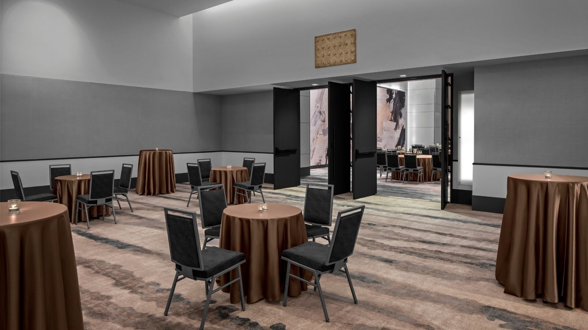 A conference room with round tables and chairs, a carpeted floor, and a large open door leading to another room.