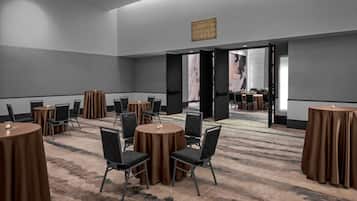 A conference room with round tables and chairs, a carpeted floor, and a large open door leading to another room.