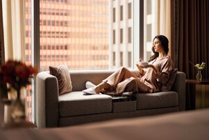 Una persona sentada en un sofá junto a una ventana con vista a la ciudad.