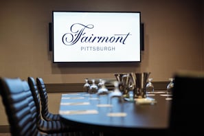 A conference room with a screen displaying "Fairmont Pittsburgh" and a table set with glasses and cutlery.